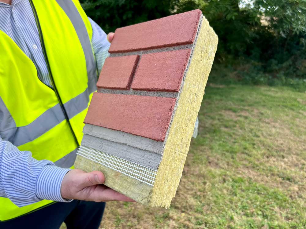 Worker in a high visibility vest holds up a panel of external wall insulation