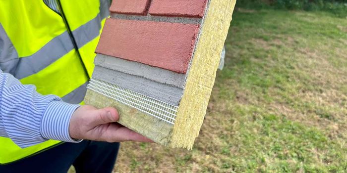 Worker in a high visibility vest holds up a panel of external wall insulation