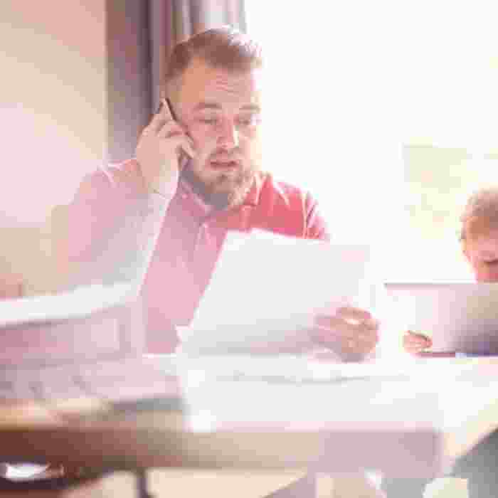Man on phone look at bills with toddler sat beside him