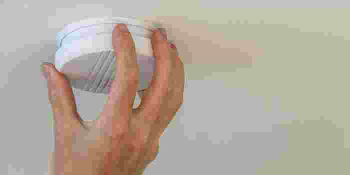 A hand on a smoke alarm fitted to the ceiling