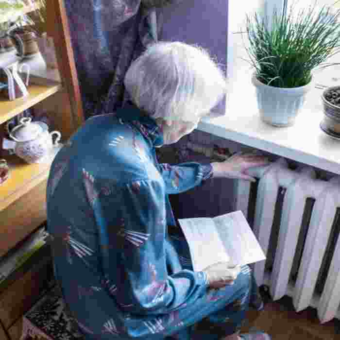 Elderly lady holds bill whilst feeling radiator with other hand