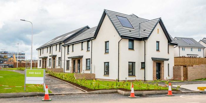 New houses with solar panels on roofs and a for sale sign outside