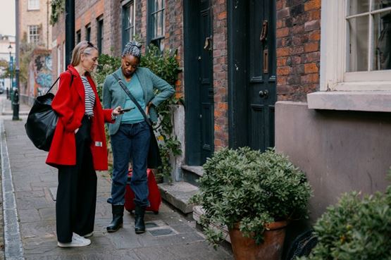 Two women looking at tablet outside houses